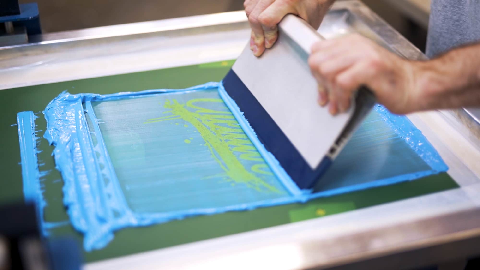 Screen print press operator demonstrating the printing stroke.