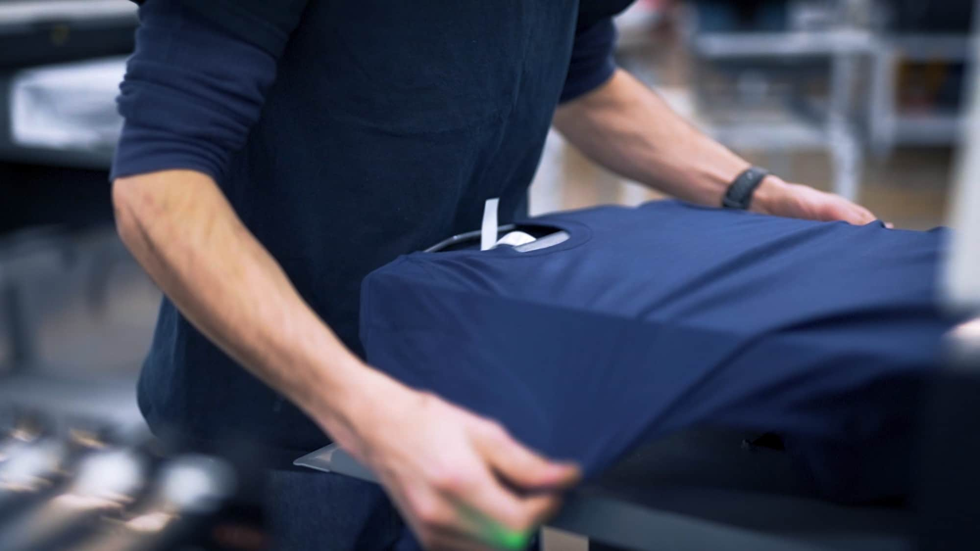 Digital printer operator demonstrating loading a blank t-shirt to be printed.