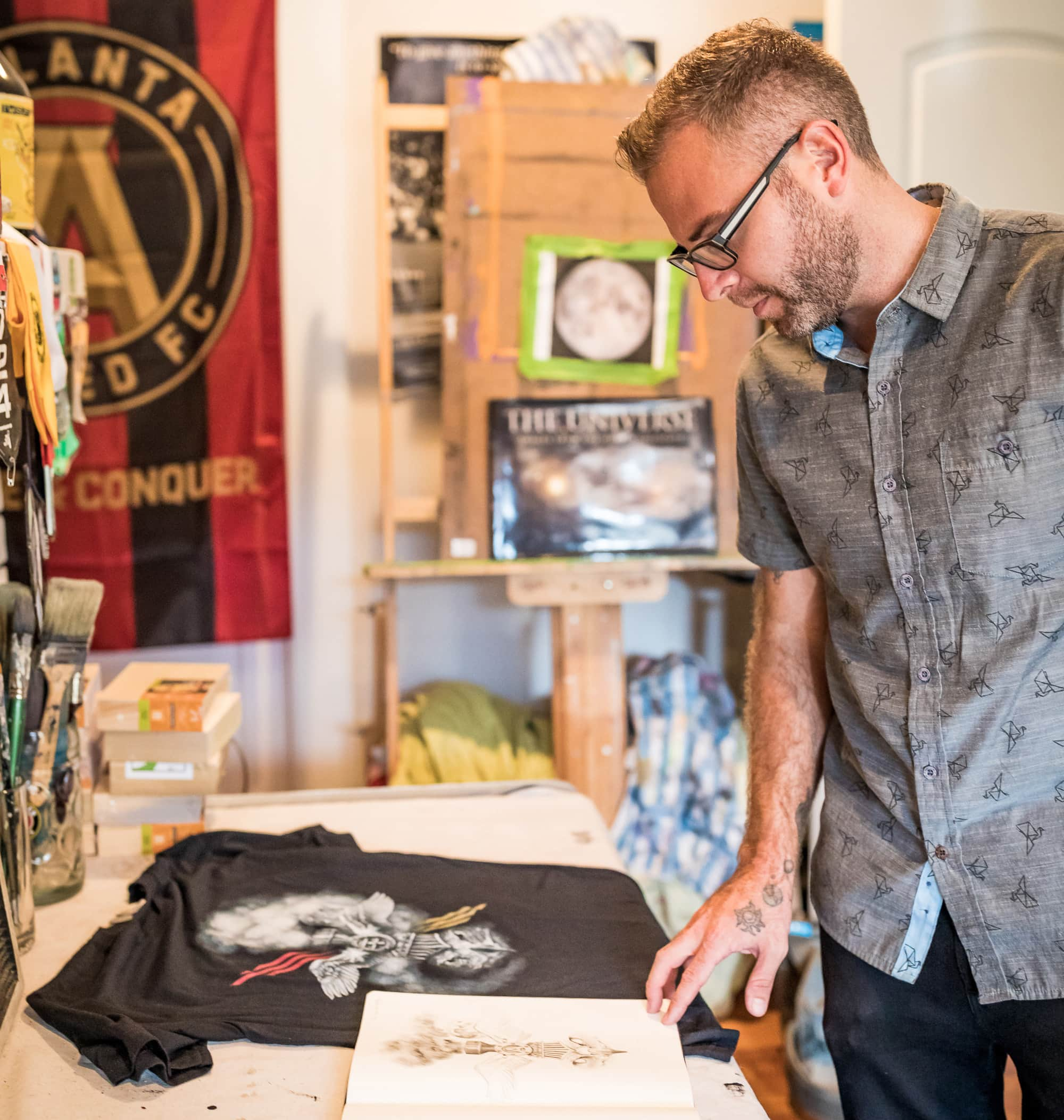 Artist Thomas Turner in his studio looking down at his sketch book and printed t-shirt.