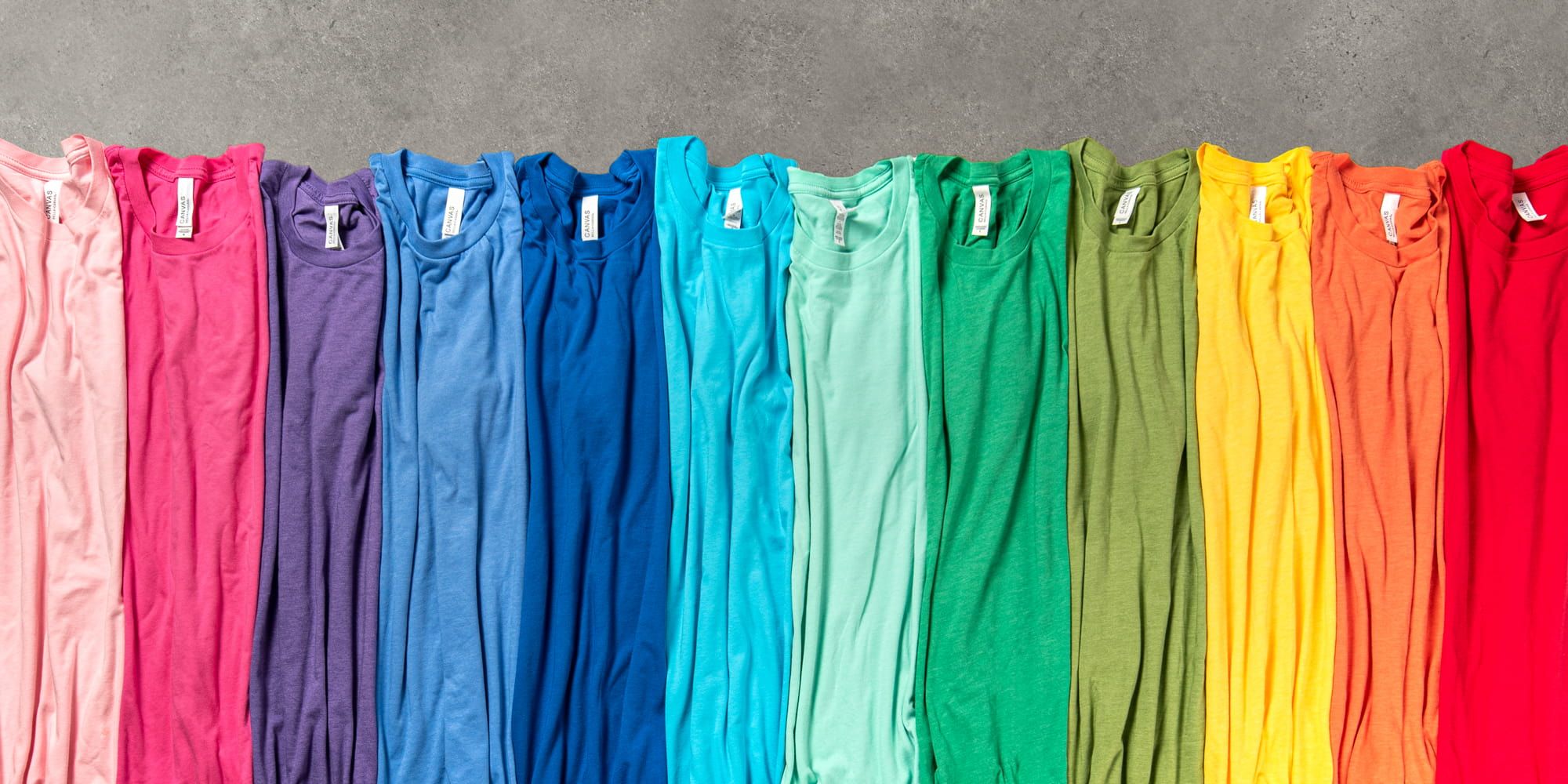 Top down image of colorful shirts side-by-side that show all the colors of the rainbow