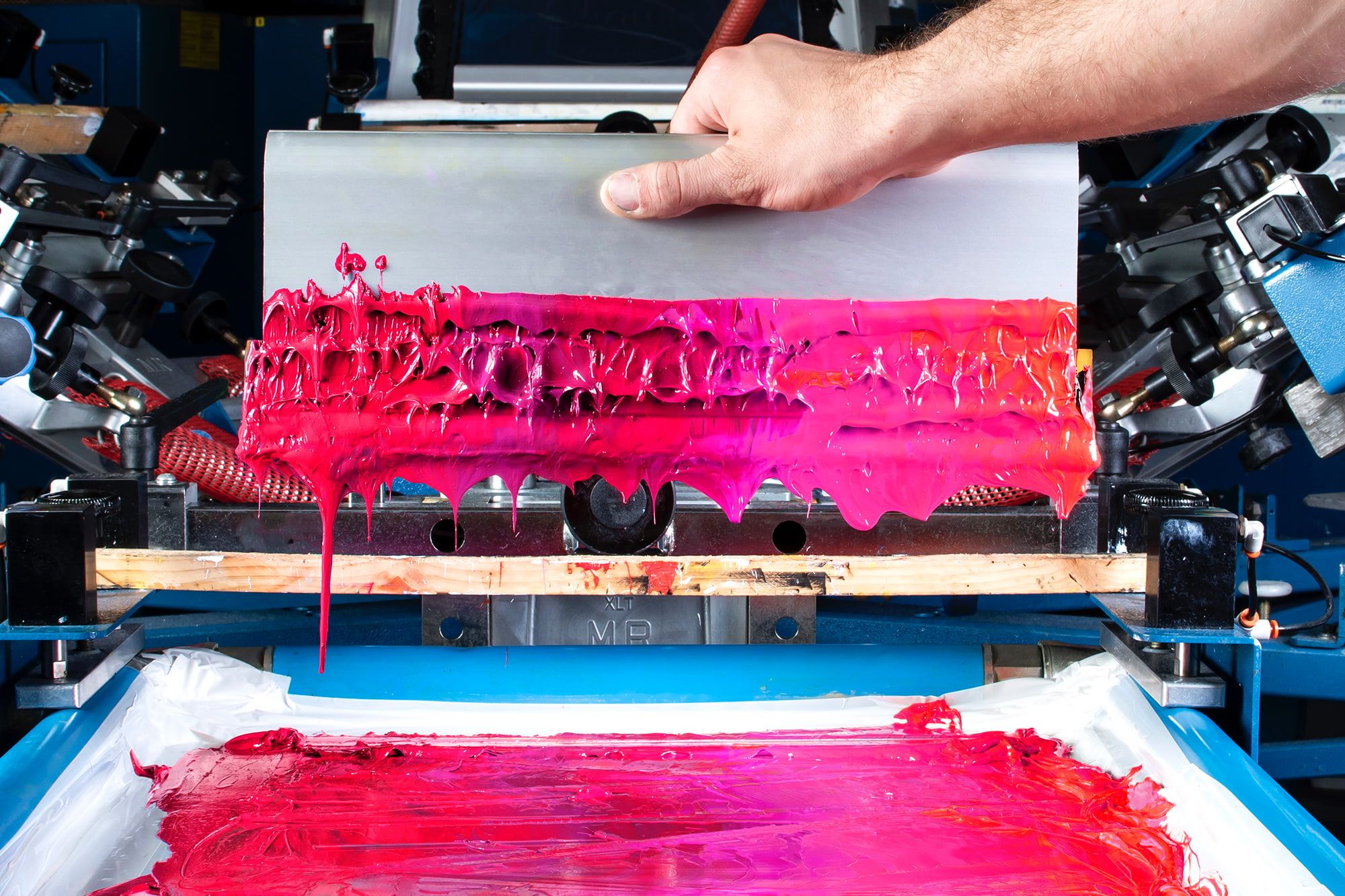 A person holding a screen printing squeegee that has been coated in a variety of magenta and dark pink inks