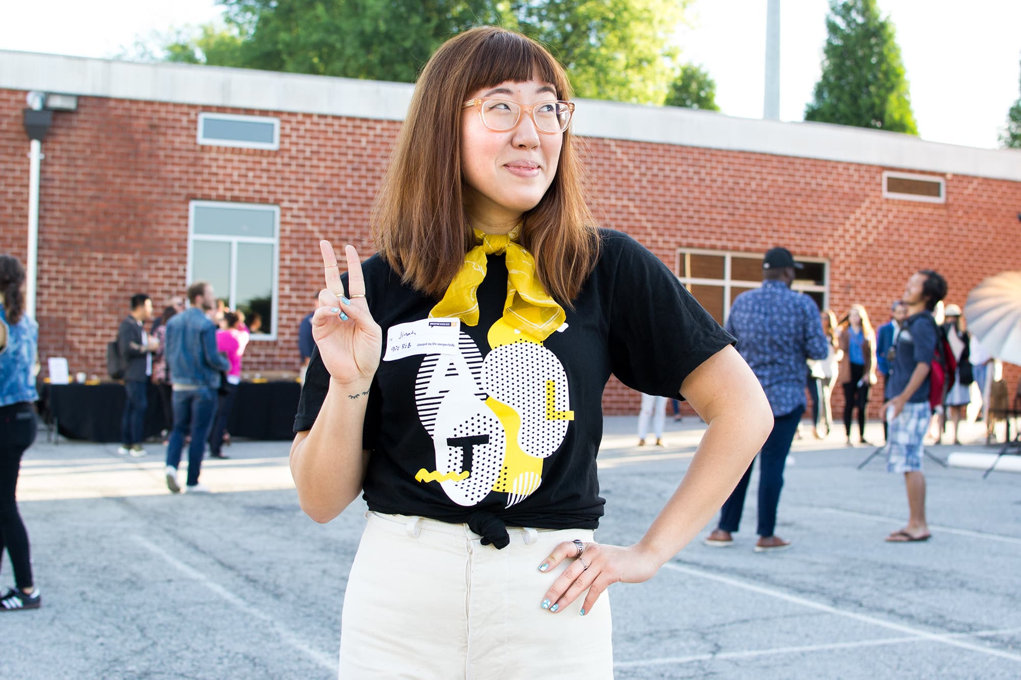 A person wearing glasses and holding up a peace sign showing off their free t-shirt they received at a local event for creatives.
