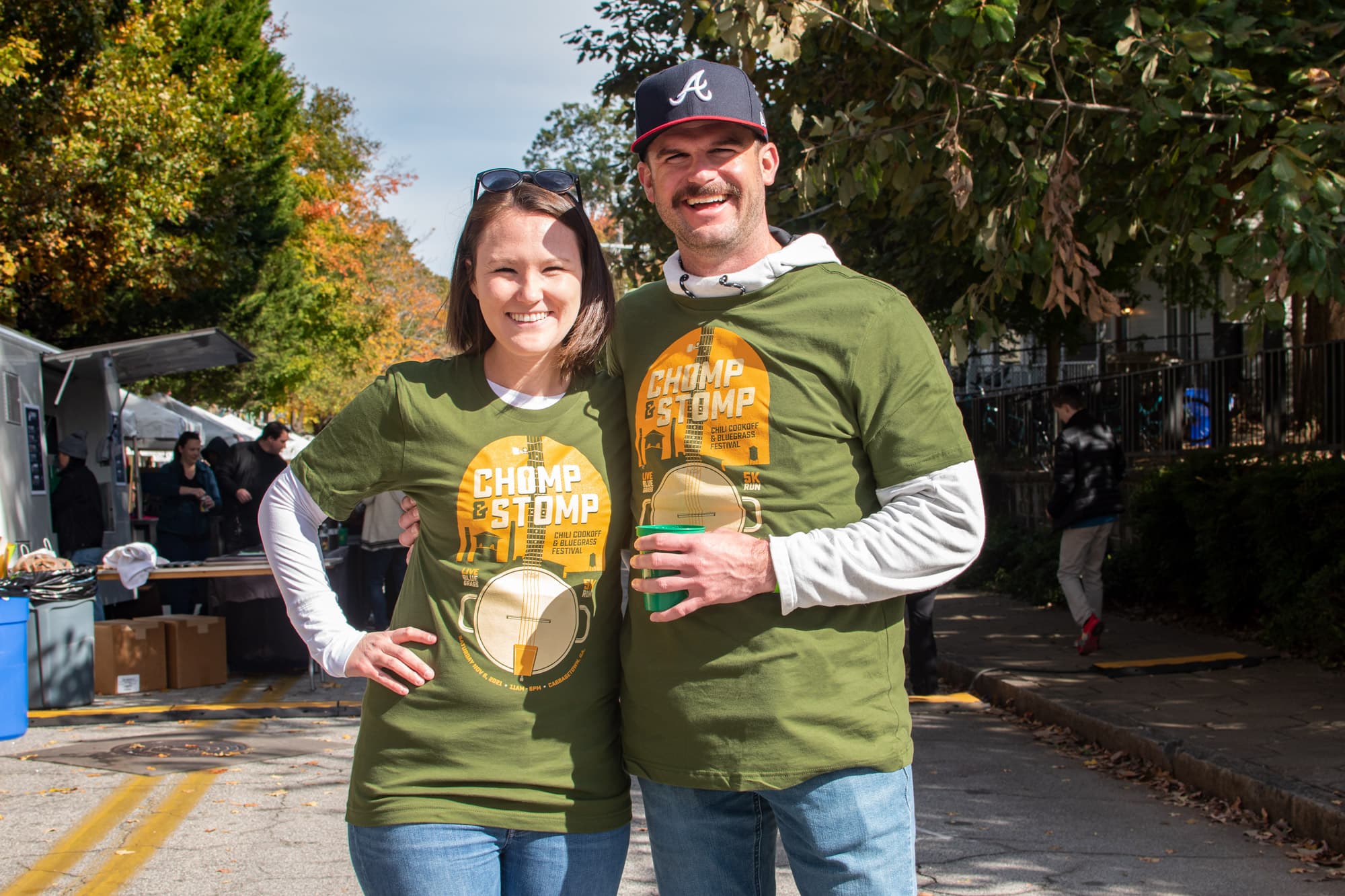 Two people wearing shirts for a local Chili Cookout and Bluegrass event stand side by side smiling. 
