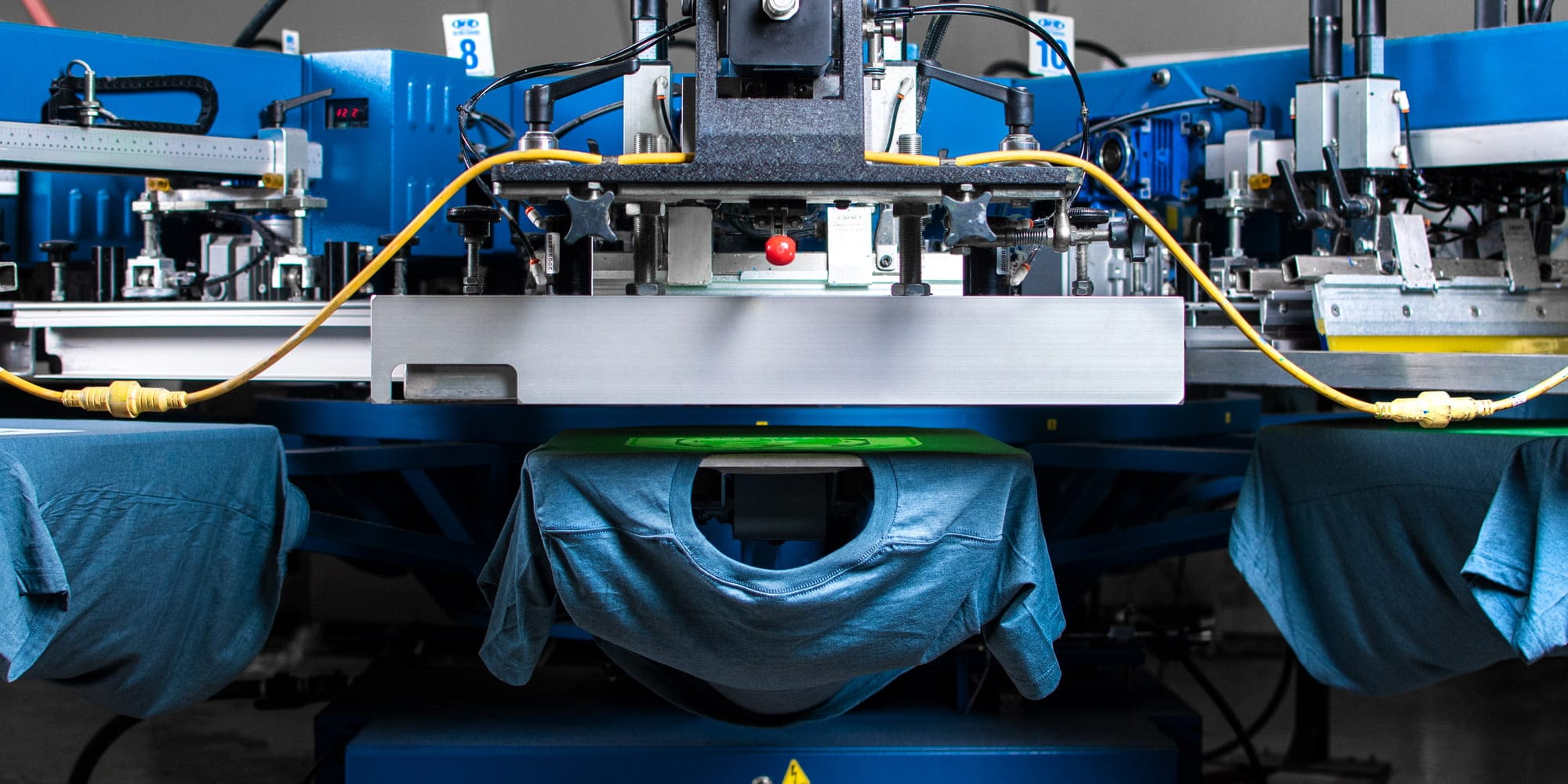 Artistic perspective of an automatic screen printing press showing shirts being printed.