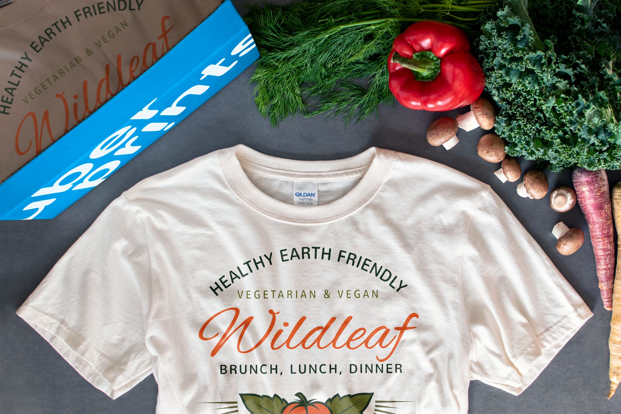 Flatlay of a t-shirt surrounded by produce that features a design for a healthy restaurant.