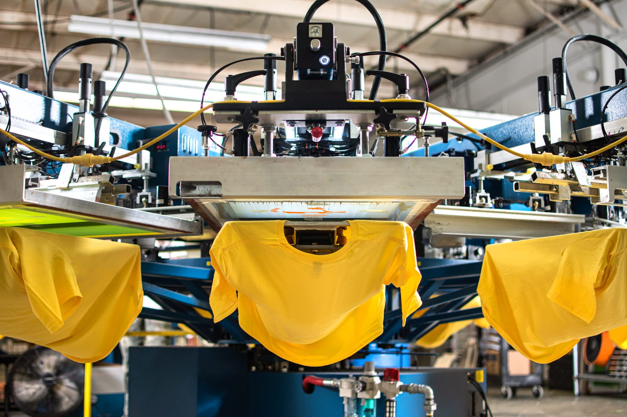 Low down angle of bright t-shirts on an automatic screen printing press ready to be printed.