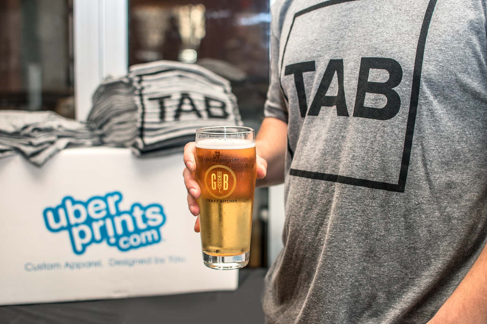 A closeup of a person holding a beer and wearing a t-shirt from a local event.