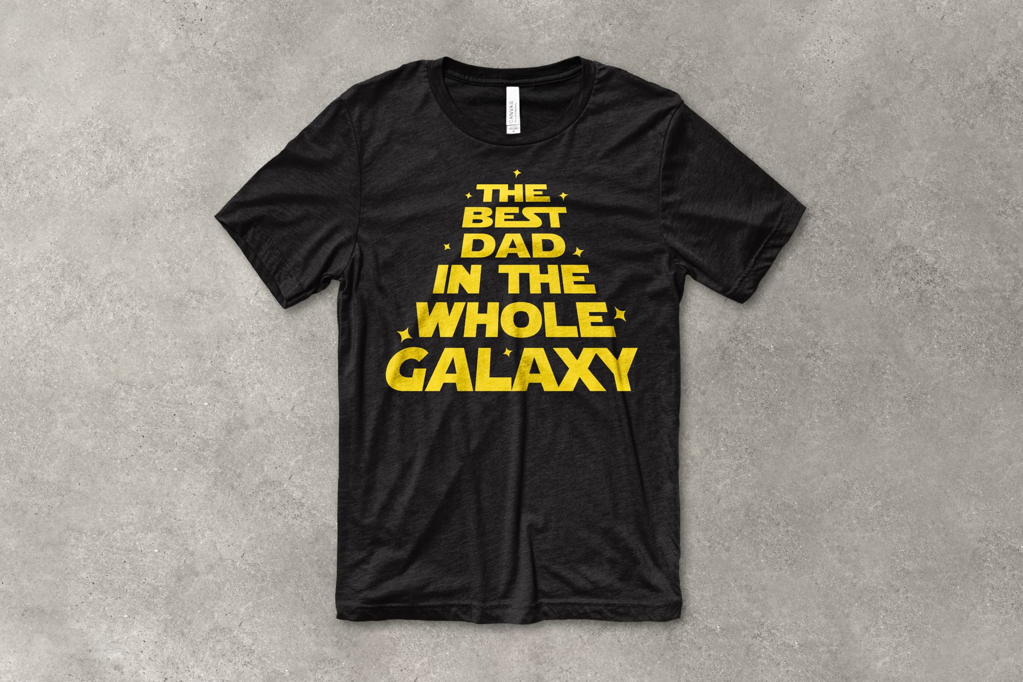 A flat t-shirt that has a customizable design that says "The best dad in the whole galaxy" in the style of Star Wars