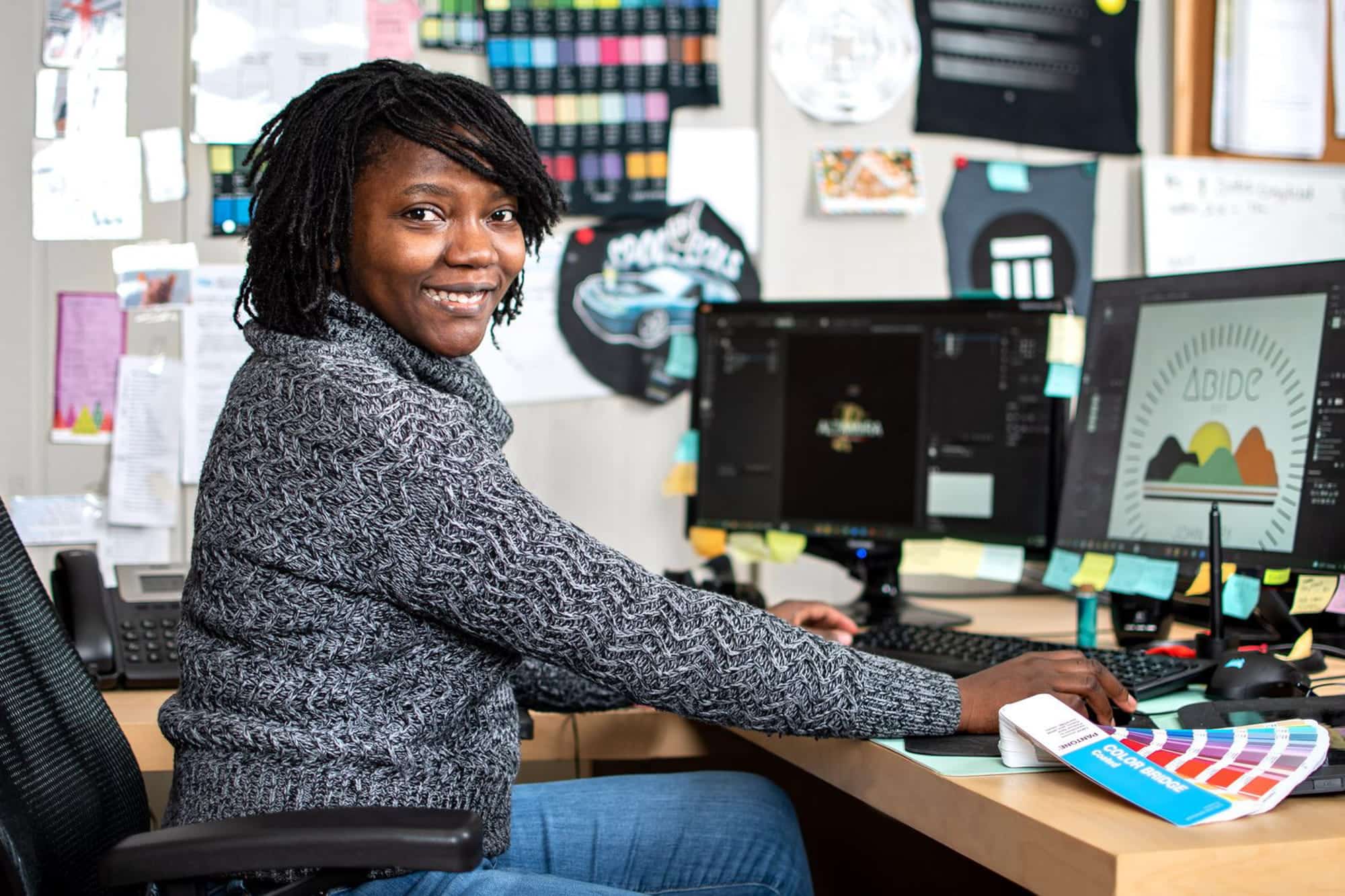 Image of a person in the art department working on a design and looking over and smiling at the camera 