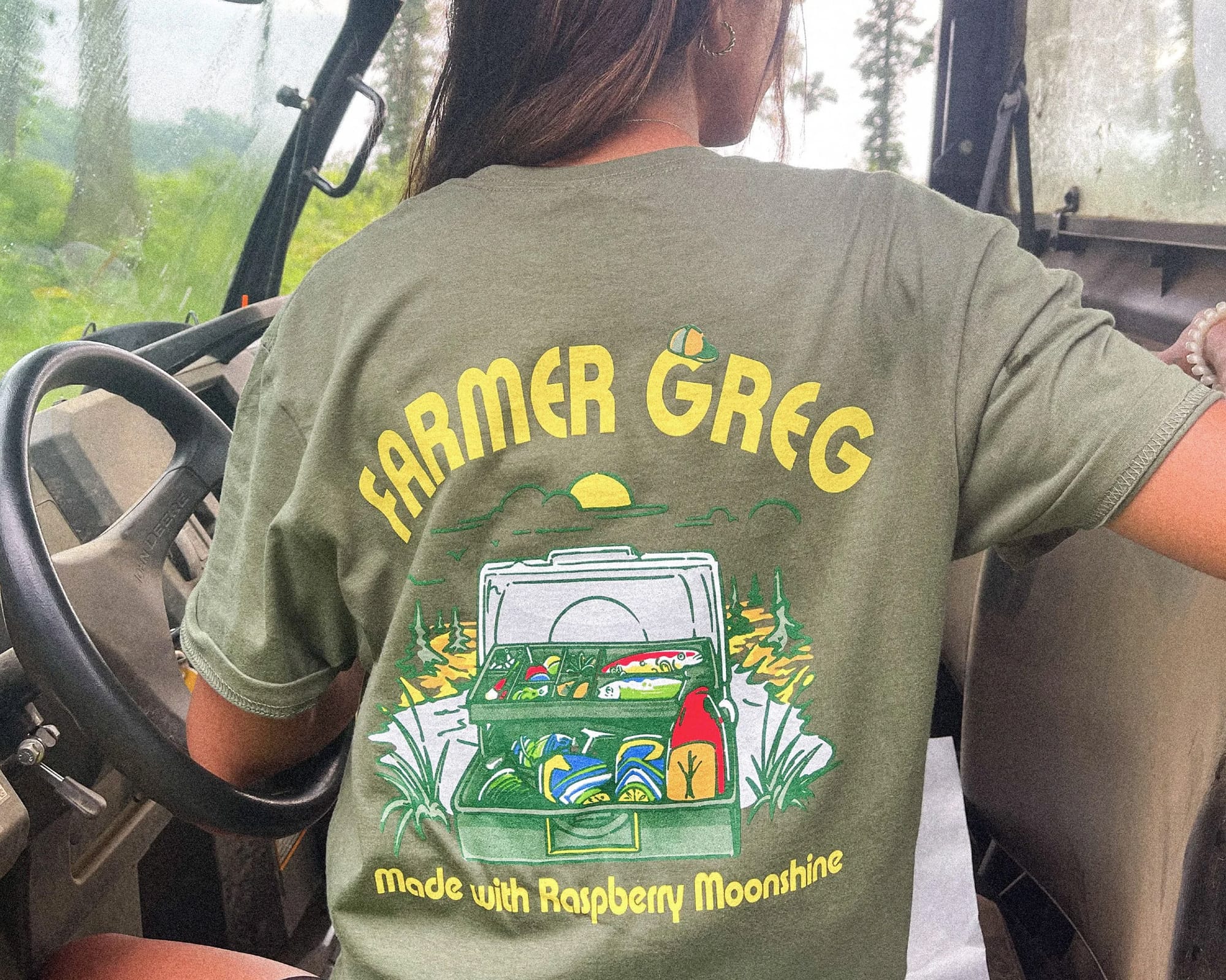 Image is of the back of a person wearing a t-shirt that says "Farmer Greg. Made with raspberry moonshine."