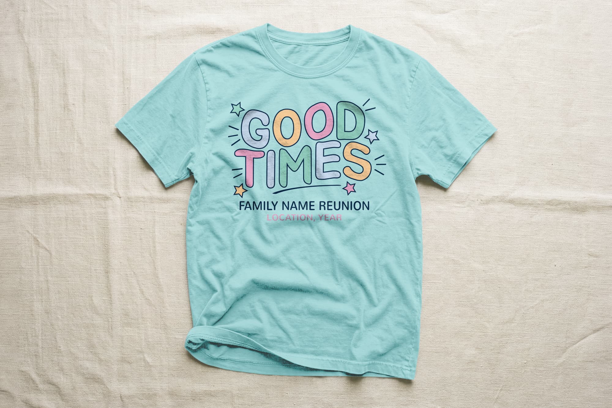 Light blue T-shirt with colorful, bold text "GOOD TIMES" surrounded by stars. Below, smaller text: "Family Name Reunion, Location, Year." Laid on a beige surface.