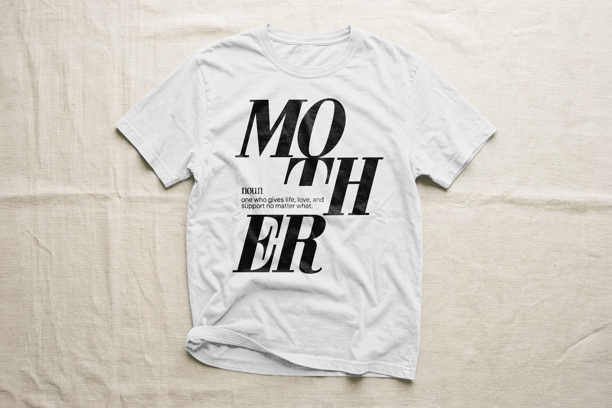 White T-shirt with bold black text "MOTHER" in a stylish font. Below, it defines "noun: one who gives life, love, and support no matter what."