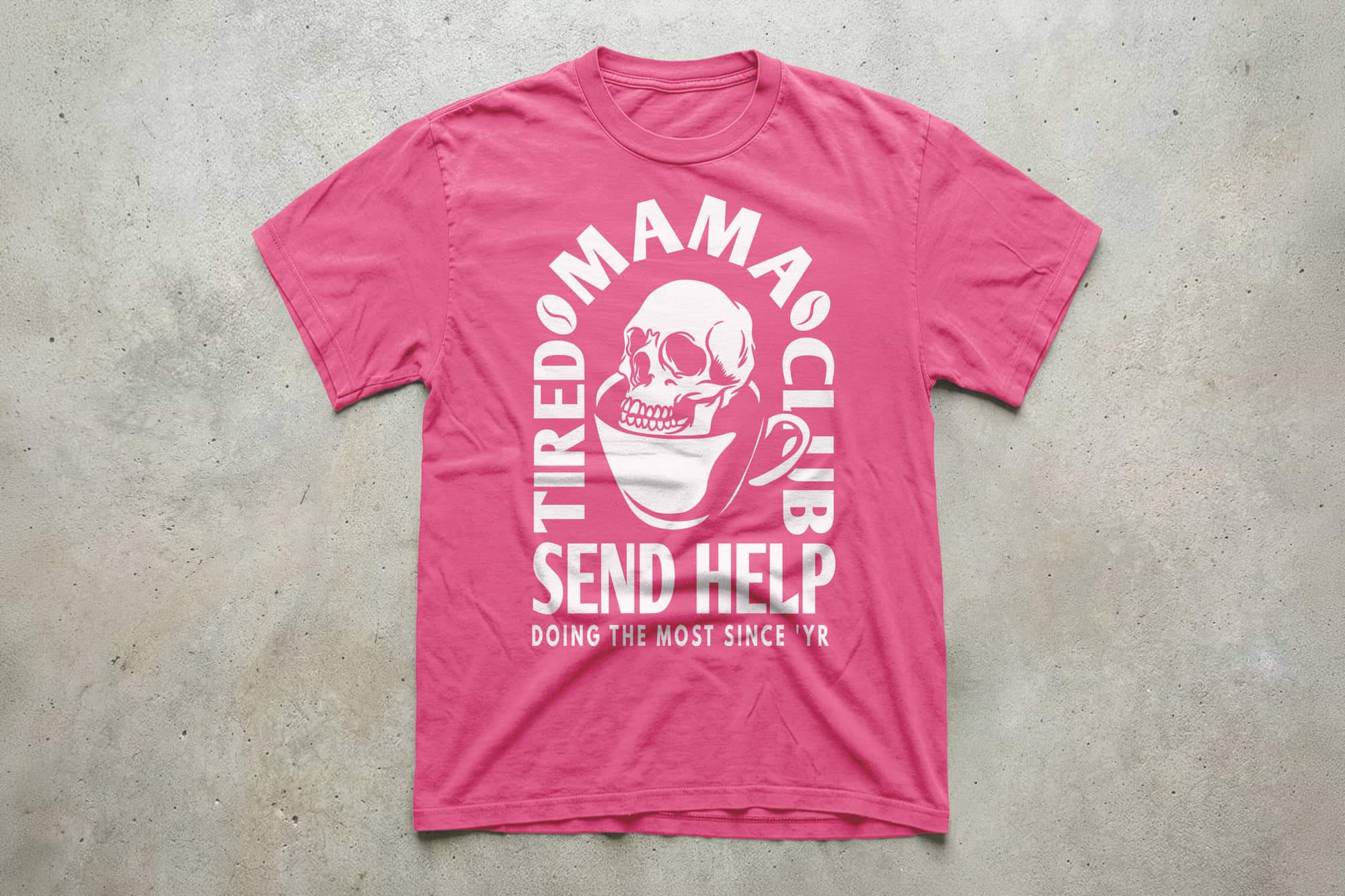 A pink T-shirt displays white text and graphics. At the center, a skull inside a coffee cup is surrounded by "Tired Mama Club." Below, it reads "Send Help." The tone is humorous.
