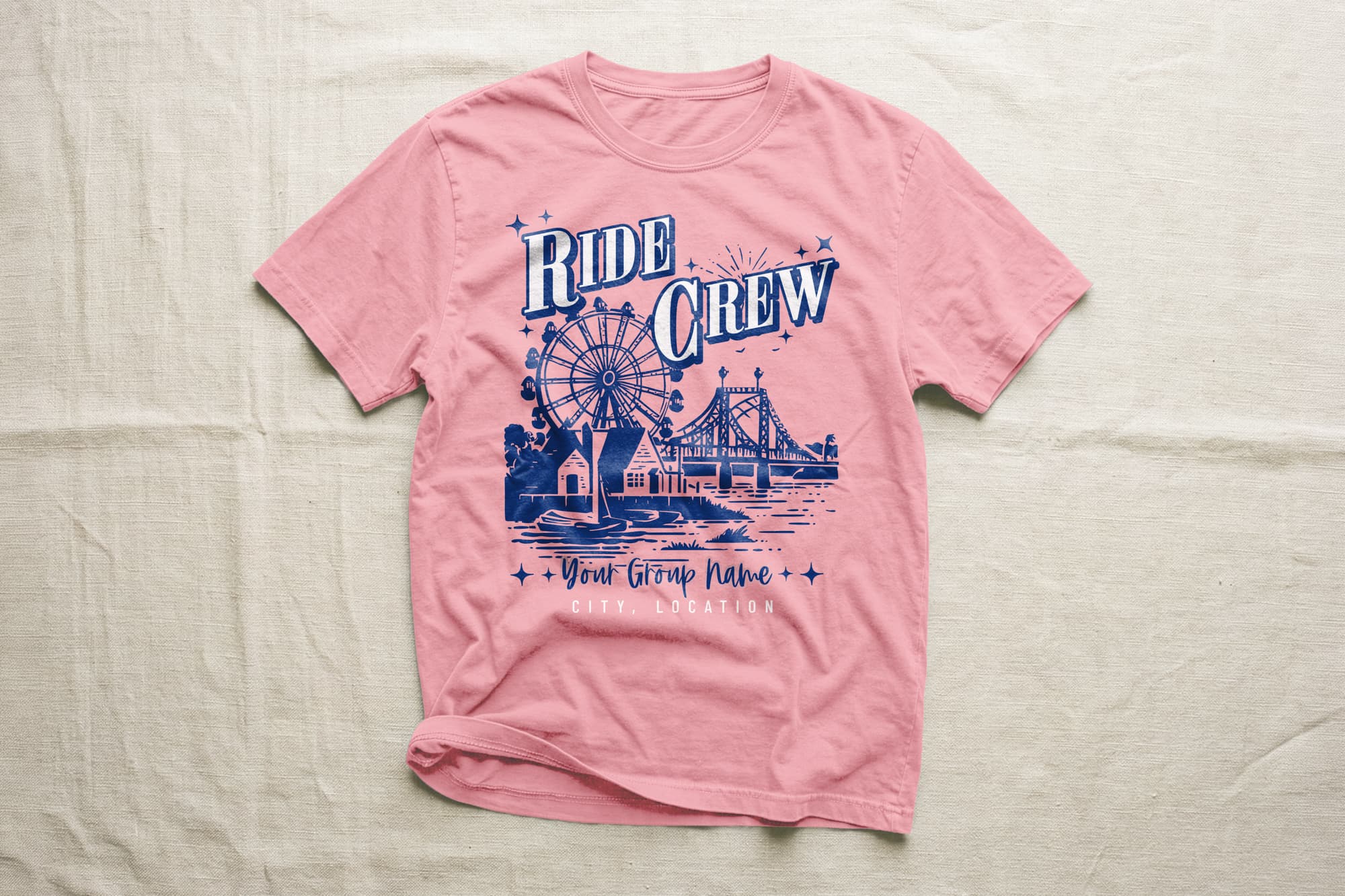 Pink T-shirt with blue graphic showing a ferris wheel, bridge, and houses. Words "Ride Crew" are prominent, with customizable text below.